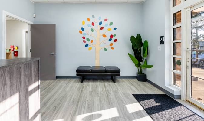A leather bench in a waiting room with a large decorative wall decor resembling a fall foliage tree. Office of Creekside Autism Center
